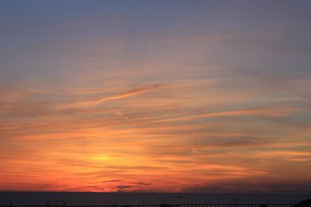 A beautiful scenery of the red horizon and cloudy sky captured during the sunsetの写真素材