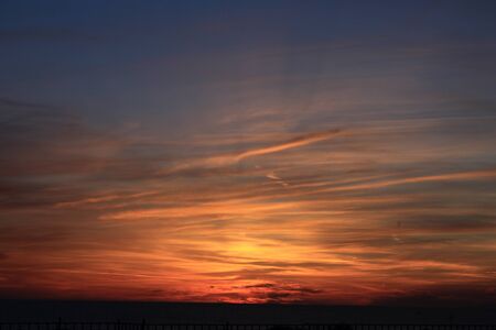 A beautiful scenery of the red horizon and cloudy sky captured during the sunsetの写真素材