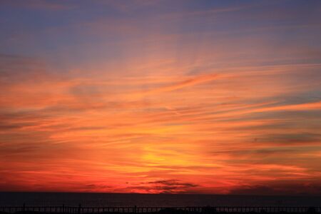 A beautiful scenery of the red horizon and cloudy sky captured during the sunsetの写真素材