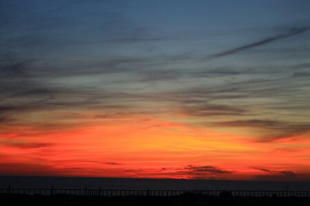 A beautiful scenery of the red horizon and cloudy sky captured during the sunsetの写真素材