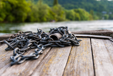 A close up of a chain on the planks of a boat navigating on the still water of Rhine river with trees on backgroundの写真素材