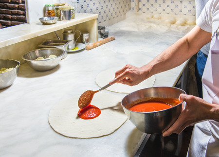 Pizza chef spreading out and garnishing a delicious pizzaの写真素材
