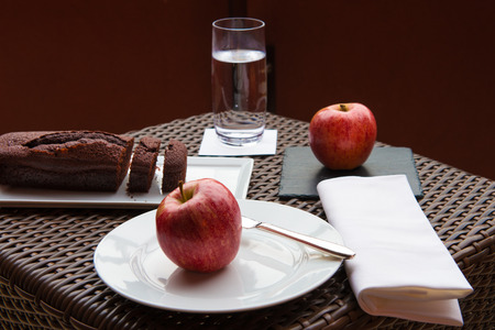 breakfast on the terrace wicker table with chocolate cake and two red applesの写真素材