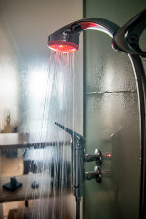 interior of a glass shower cabin with running water and moisture on glass. shower head has colored lightの写真素材