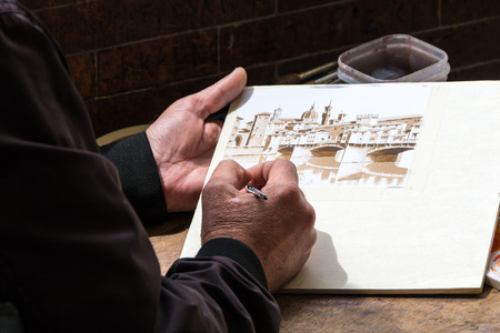 Detail of the hands and tools of a street artist who paints Ponte Vecchio in Florence, warm colorsの写真素材