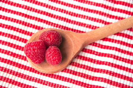 Pink raspberries in a wooden spoon on a red-white striped background from above