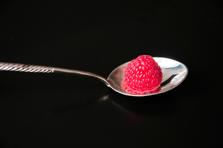 A raspberry on a silver spoon on a black backgroundの写真素材