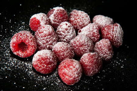 Beautiful red raspberries with a sugar powder on a black backgroundの写真素材