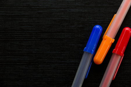 Red, orange and blue pens on black background, copy space