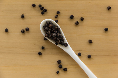 Black pepper in white spoon on wooden backgroundの写真素材