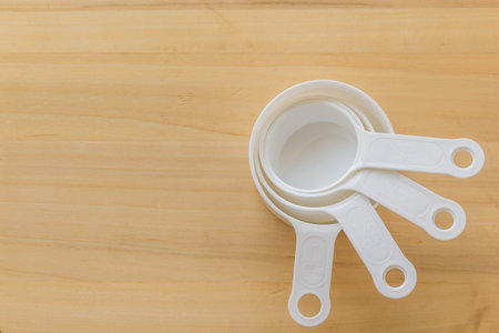 White plastic measuring cup on wooden background, copy space