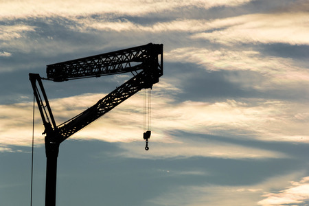 Silhouette tower crane with hook on blue sky background, industrial conceptの写真素材