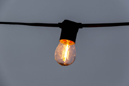 Single light bulb hanging on black cable with blue background