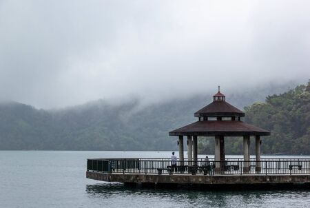 Pavilion at Sun Moon Lake in tranquil atmosphere with mist and mountain backgroundの写真素材