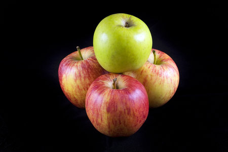 Green apple on red apples on a black background