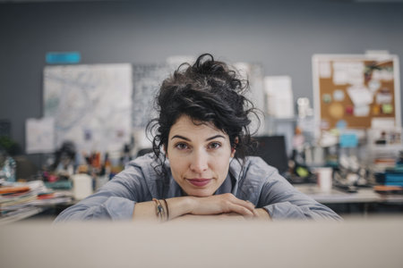 A focused female professional with curly hair rests her chin her hands office settingの素材