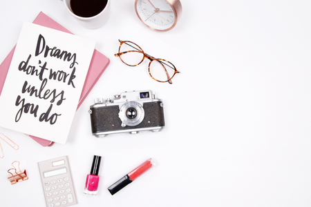 Women's home office desk workspace with handwritten quote notebook, retro camera, smartphone, lipstick and coffee cup on white background. Flat lay, top view. Creative stylish blogger concept.の写真素材
