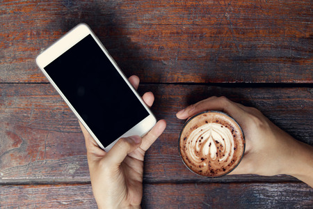 Close-up image of woman or male hands using smartphone at cafe while drinking coffee. Typing text message, via cell phone, Social networking concept. Smartphone mockup.の写真素材