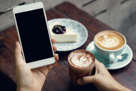 Close-up image of woman or male hands using smartphone at cafe while drinking coffee. Typing text message, via cell phone, Social networking concept. Smartphone mockup.の写真素材