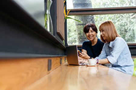 Smiling small business owners woman discussing ideas for project sharing opinions and checking business plan on laptop while sitting at cafe. Copy space, Selective focus.の写真素材
