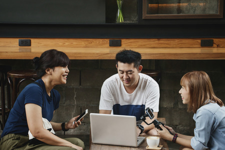 Cheerful male and female blogger discussing ideas for new project, brainstorming and checking video clip on laptop while sitting at cafe.の写真素材