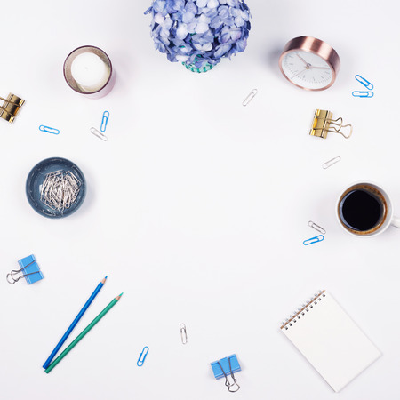 Flat lay, Top view office table desk. Feminine desk workspace frame with beauty arrangement of bouquet hydrangeas, notebook, clips, clock, pencil and candle on white background.の写真素材