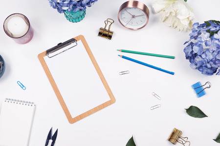 Flat lay, Top view office table desk. Feminine desk workspace frame with beauty arrangement of bouquet hydrangeas, notebook, clips, clock, pencil and candle on white background.の写真素材