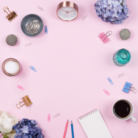 Flat lay, Top view office table desk. Feminine desk workspace frame with beauty arrangement of bouquet hydrangeas, notebook, clips, clock, pencil and candle on pink background.の写真素材