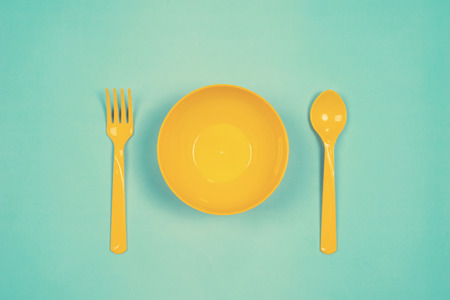 Set of empty yellow plastic tableware bowls, yellow spoons and forks  isolated on green background. Flat lay, Top view. Minimal style.の写真素材