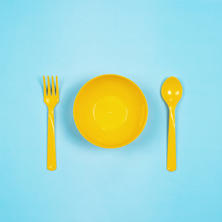 Set of empty yellow plastic tableware bowls, yellow spoons and forks  isolated on blue background. Flat lay, Top view. Minimal style.の写真素材