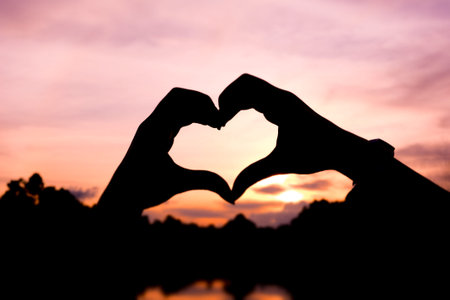 Hands and fingers in heart shape framing at sunsetの写真素材