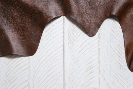 Natural brown cow leather on the white wooden boards. May used as background.