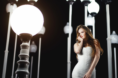 Beautiful model girl in white dress looking at bright light with lanterns at background.の写真素材