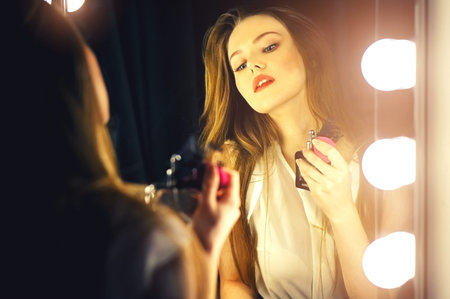 Beautiful sexy young woman looking into a mirror at herself and use perfume on her neck.
