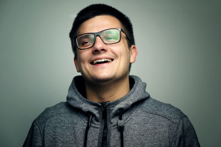 Smiling young handsome man in sport wear with glasses looking away in studio. Grey isolated background.の写真素材