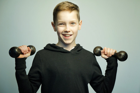 Portrait of a handsome teenage sport boy with dumbbells and stylish haircut, softbox lighting studio shot.の写真素材