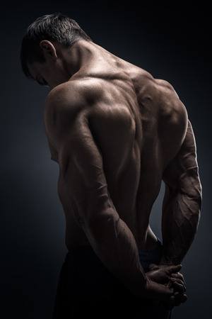 Handsome muscular male model bodybuilder preparing for fitness training turned back. Studio shot on black background.