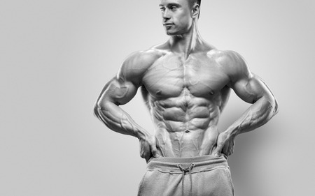 Handsome power athletic young man with great physique. Strong bodybuilder with six pack perfect abs shoulders biceps triceps and chest. Studio shot on white backgroundの写真素材