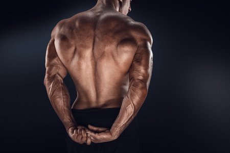 Handsome power athletic man showing his back. Strong bodybuilder with shoulders biceps triceps and chestの写真素材