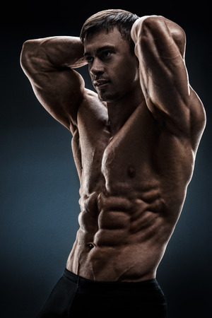 Powerful shirtless male bodybuilder posing over black backgroundの写真素材