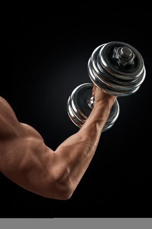 Closeup of a handsome power athletic man bodybuilder doing exercises with dumbbell. Fitness muscular body on dark background.の写真素材