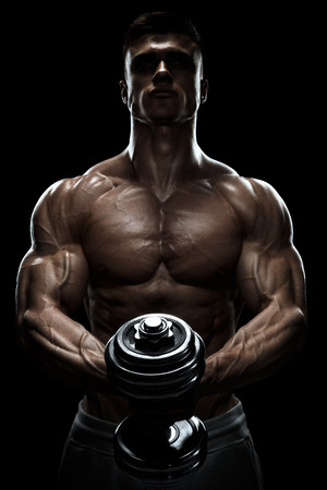 Silhouette of a bodybuilder. Power athletic man pumping up muscles with dumbbell. Confident young fitness man with strong core muscles, power hands and clenched fists. Dramatic light.の写真素材