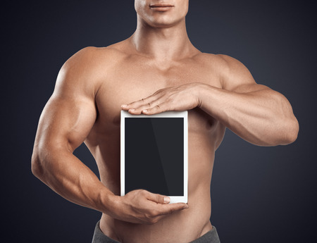 Close up photo of a handsome young fitness male model holding vertically digital tablet with blank screen, isolated on white backgroundの写真素材