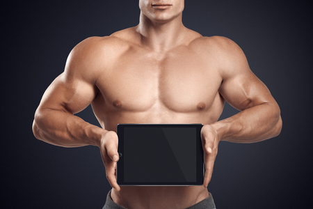 Close up photo of a handsome young fitness male model holding horizontally digital tablet with blank screen, isolated on white backgroundの写真素材
