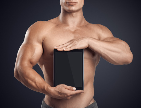 Close up photo of a handsome young fitness male model holding vertically digital tablet with blank screen, isolated on white backgroundの写真素材