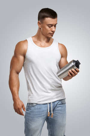 Muscular fitness male bodybuilder holding protein shake bottle ready for drinking. Studio shot on white background.の写真素材