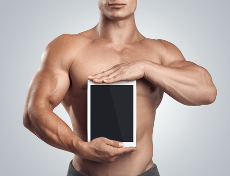 Close up photo of a handsome young fitness male model holding vertically digital tablet with blank screen, isolated on white backgroundの写真素材