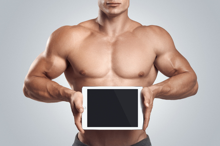 Close up photo of a handsome young fitness male model holding horizontally digital tablet with blank screen, isolated on white backgroundの写真素材