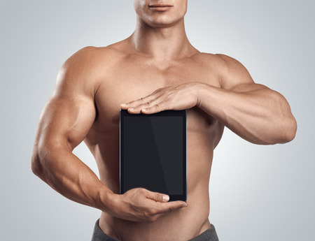 Close up photo of a handsome young fitness male model holding vertically digital tablet with blank screen, isolated on white backgroundの写真素材