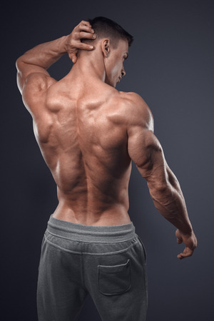 Handsome power athletic man turned back. Isolated over black background. Strong bodybuilder with shoulders, biceps, triceps and chestの写真素材